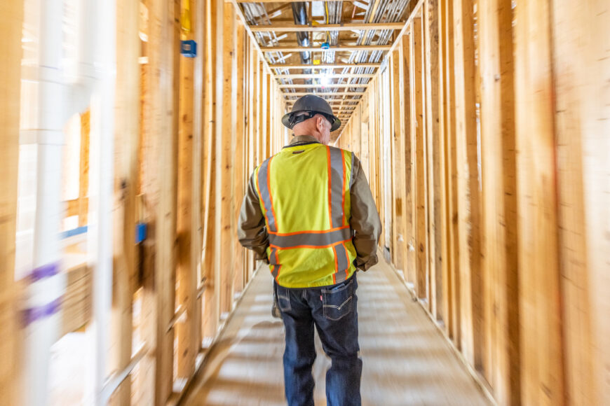 Construction worker in high-vis jacket walking between wood framing