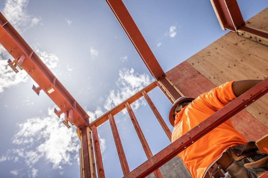 Construction worker leaning against structure with blue sky above