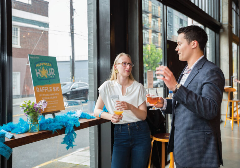 Two people talk with Make-A-Wish designs featured in background